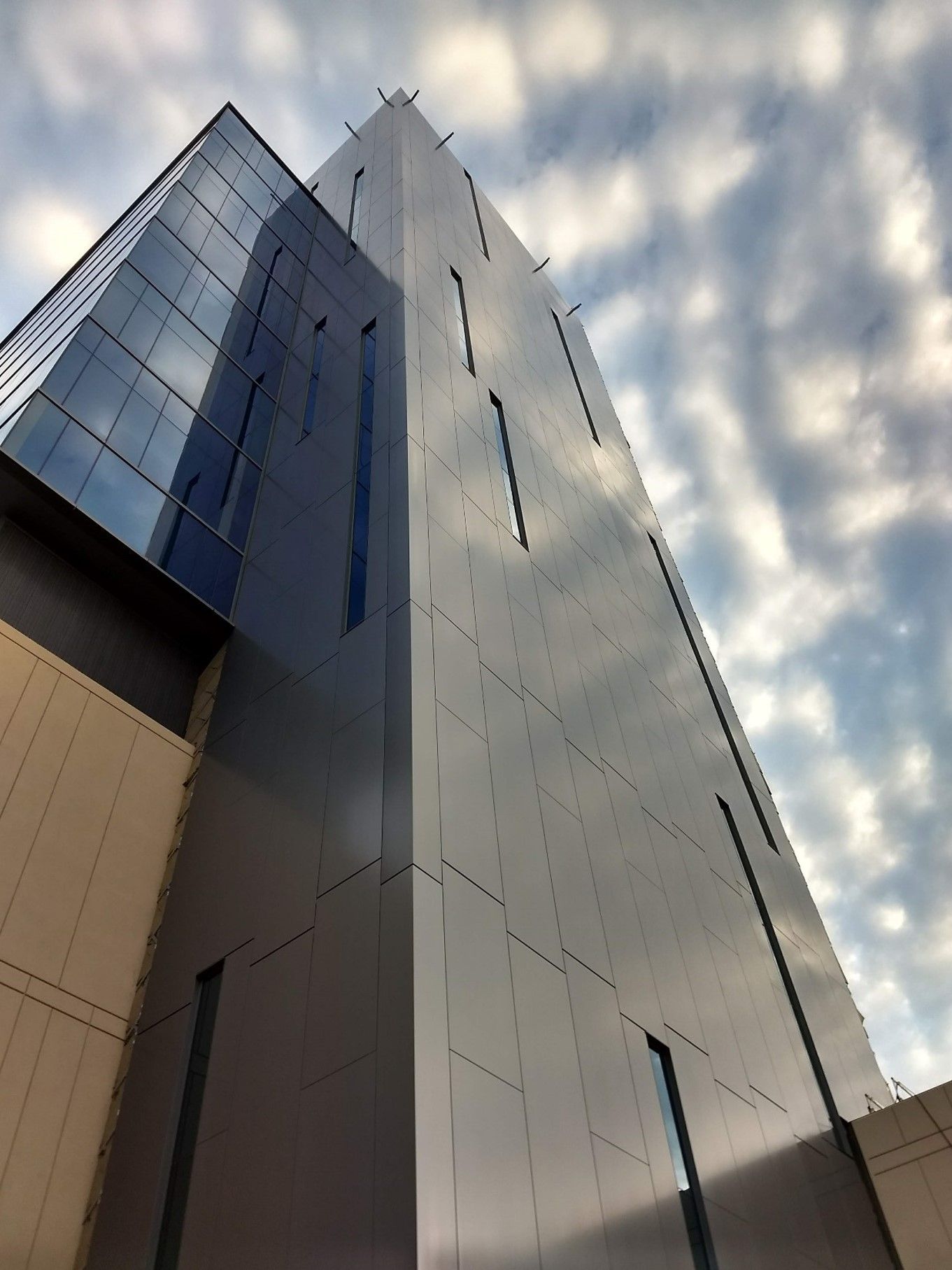 Modern building with glass and gray metal facade against a cloudy sky.