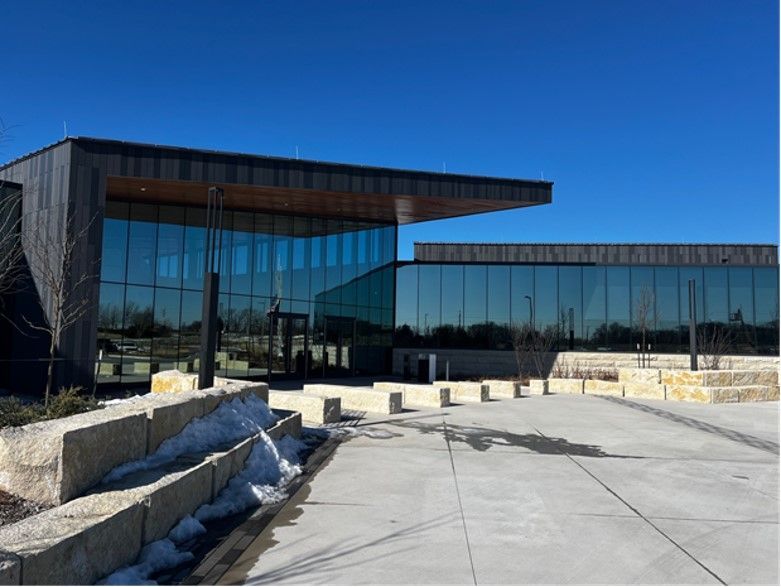 Modern building with large glass windows, a dark facade, and a flat roof against a clear blue sky.