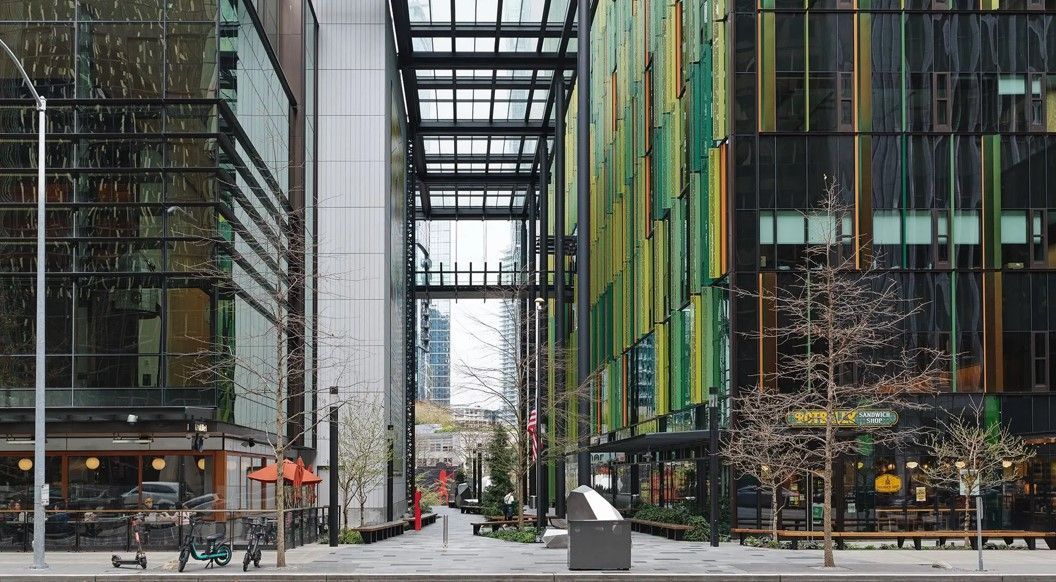 Street view of buildings. Colorful green facade on right, glass building on left. Metal framework overhead.