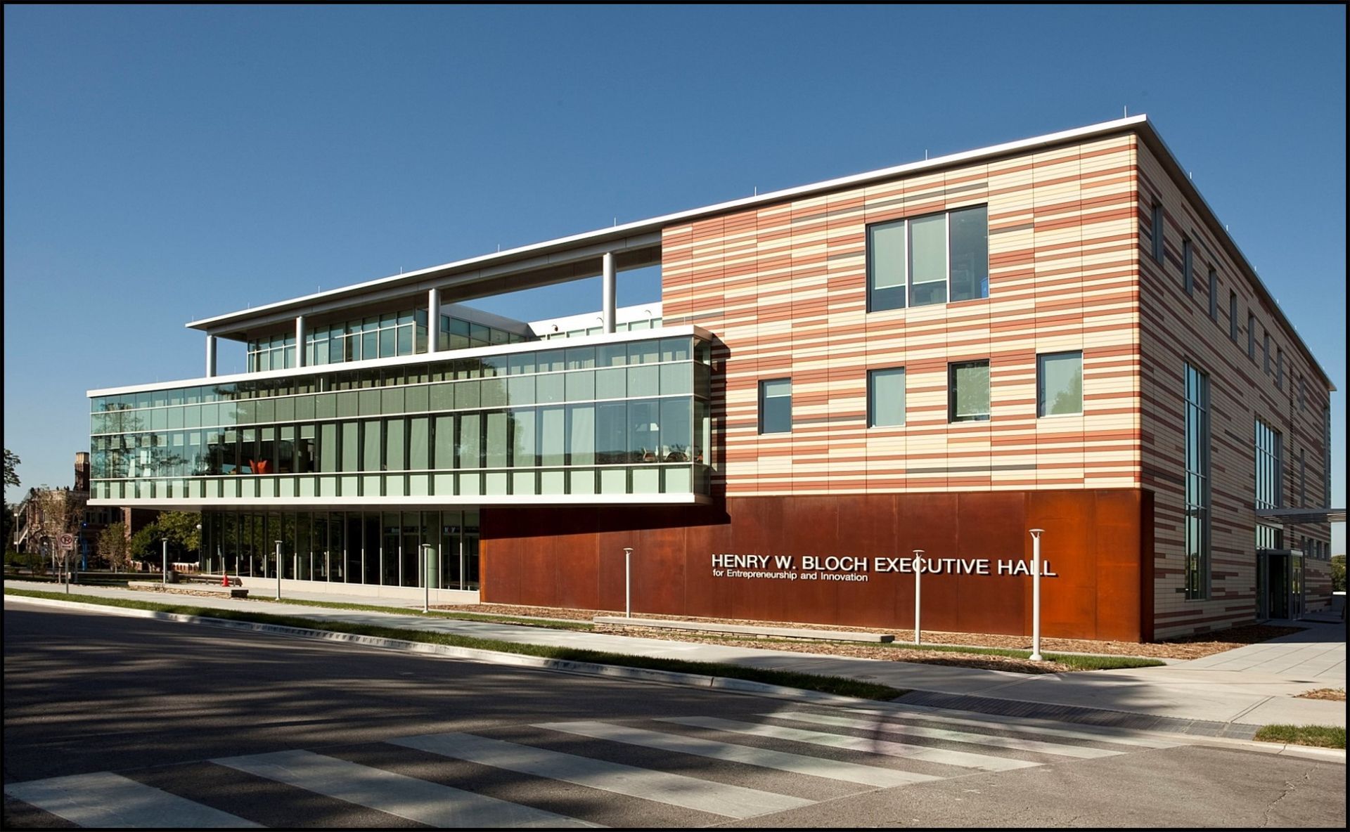 Modern building with glass and rust-colored exterior, under blue sky.