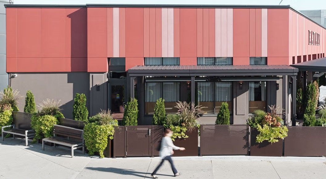 Restaurant exterior with red and brown facade, outdoor seating, and a person walking in front.