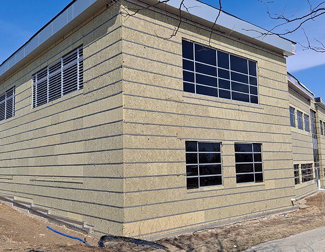 Building exterior with tan siding and dark-framed windows under a clear sky.