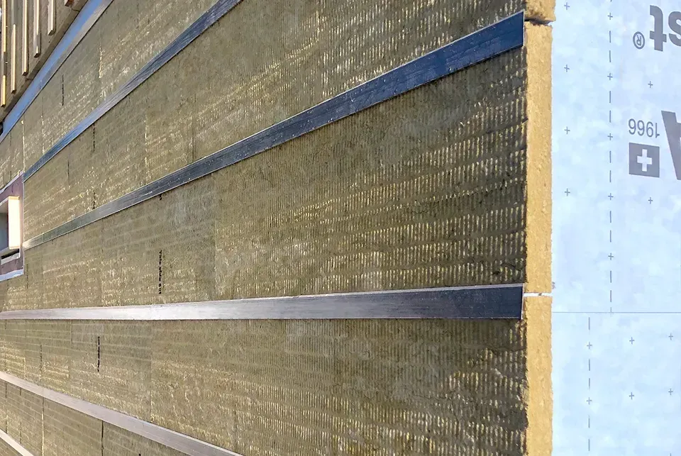 Exterior wall under construction, showing insulation panels with horizontal metal strips.