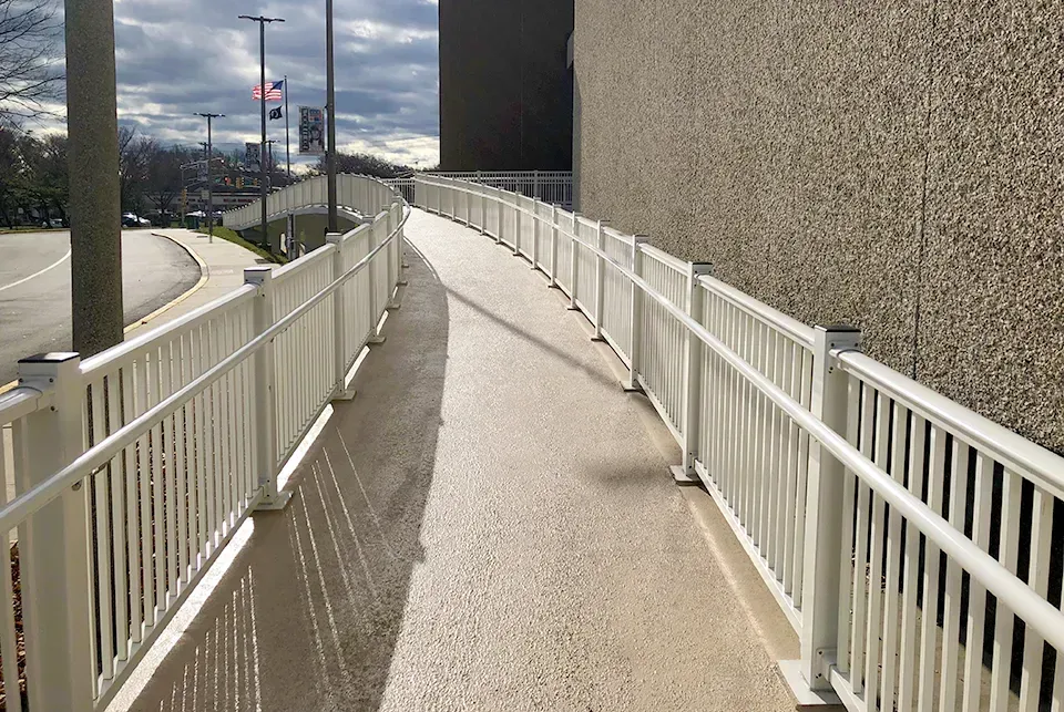 White ramp with railings extending from a building, curving toward a road with flags in the distance.