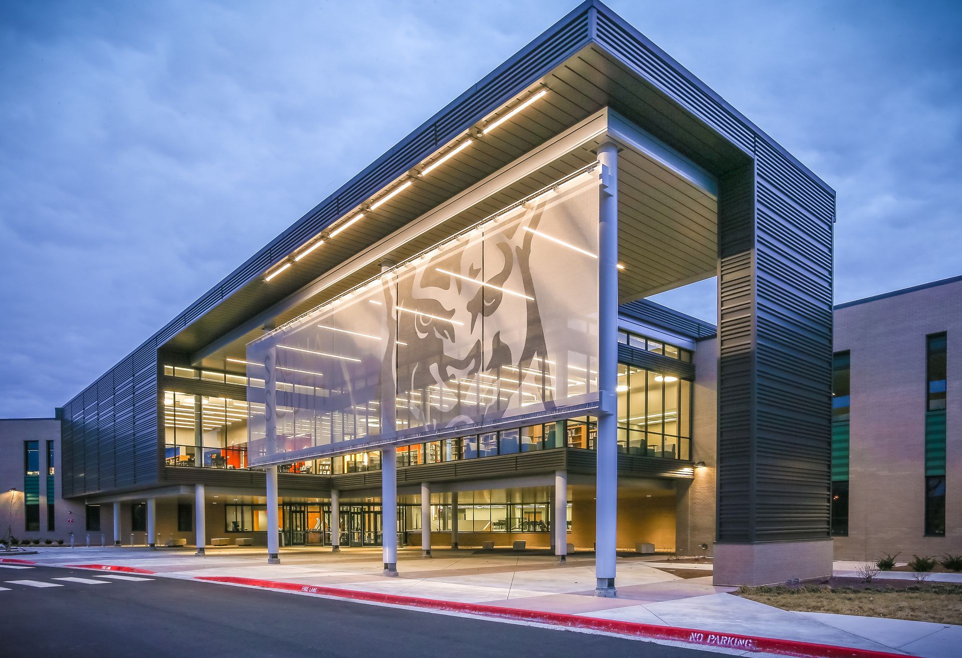 Modern building entrance with metal facade and glass windows. Lit with soft lighting at dusk.