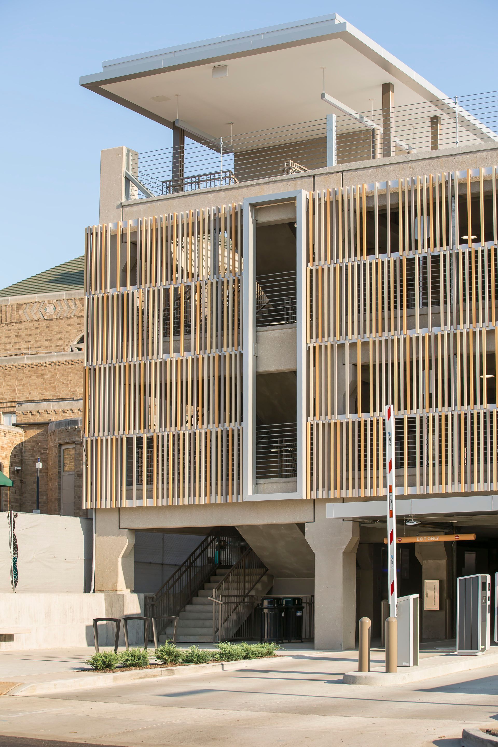 Multi-story parking garage with wooden slat facade. Entry gate, stairs, and a flat rooftop are visible.
