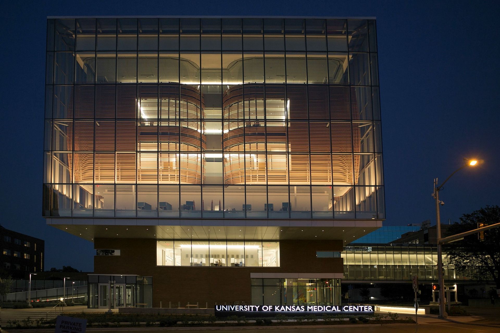 Modern glass and wood building illuminated at night; University of Kansas Medical Center sign visible.