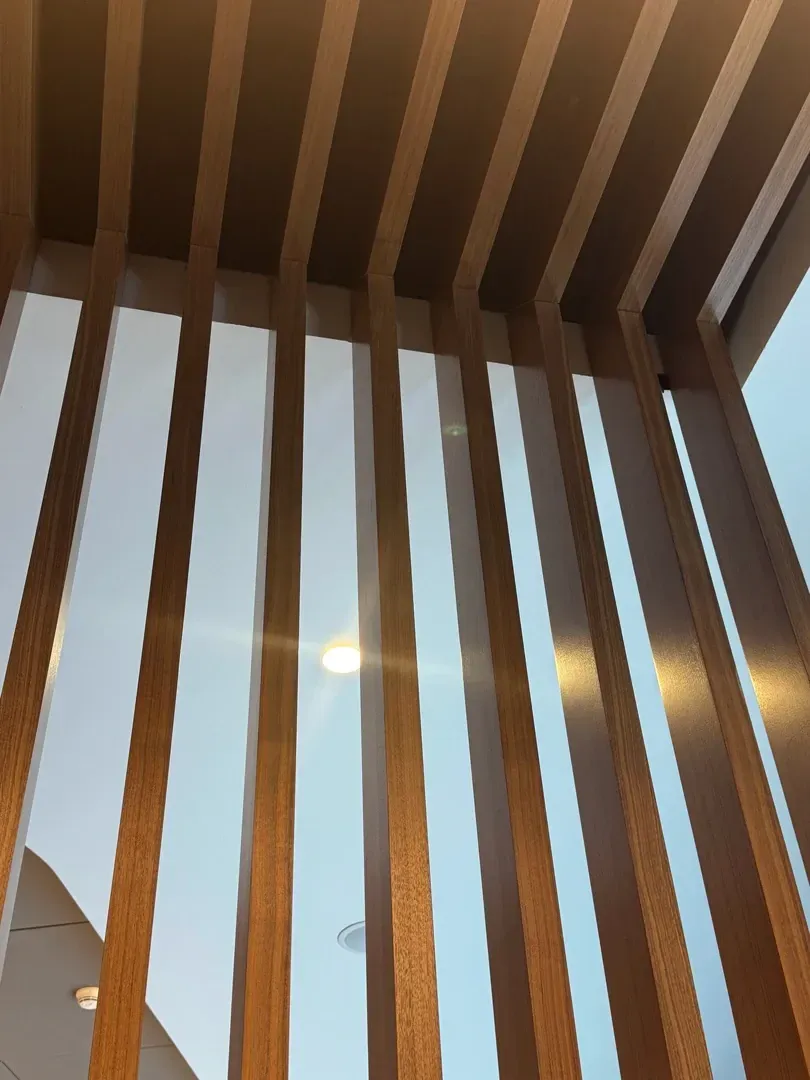 Wooden slats forming a partial wall, with glimpses of a light-filled space beyond.