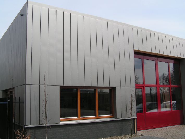 Gray industrial building with red garage door and wooden-framed windows.