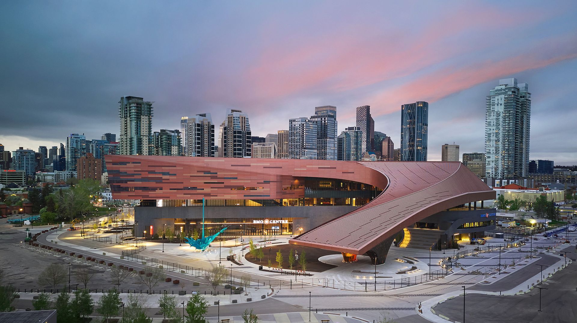 Modern building with copper facade and curved roof, downtown cityscape backdrop at dusk.