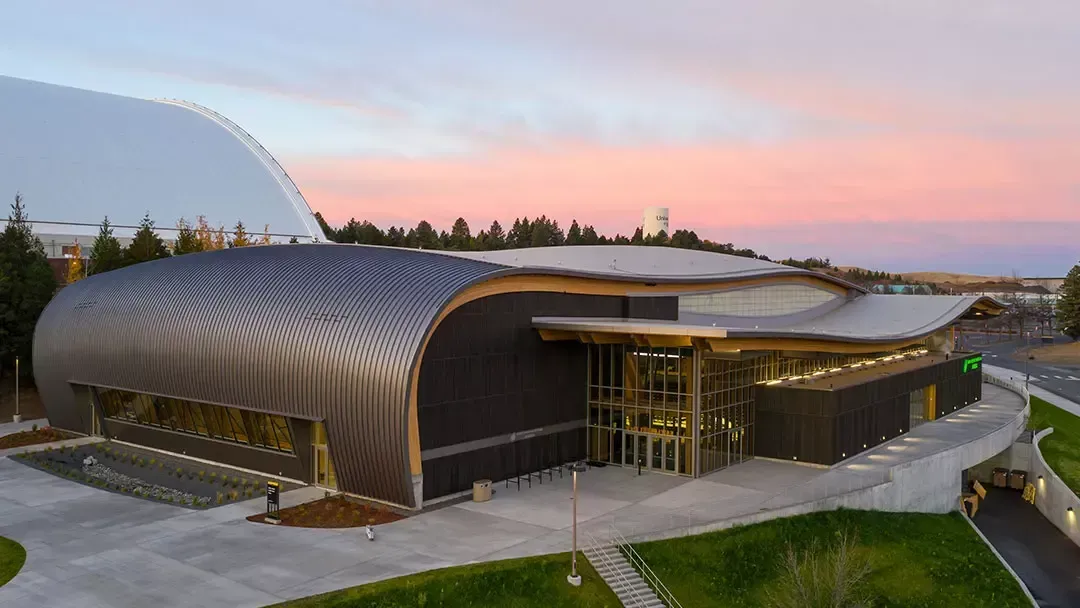Modern building with curved, patterned metal facade and glass entrance, at sunset.