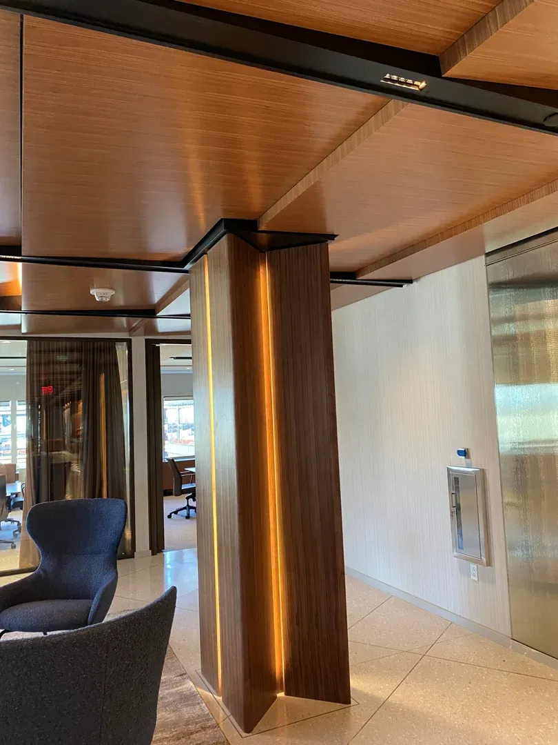 Lobby with a dark wood column lit with vertical light strips. Brown ceiling and patterned floor.