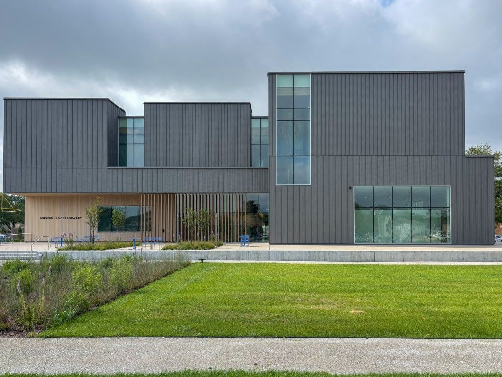Modern gray building with rectangular blocks, glass windows, and a grassy lawn.