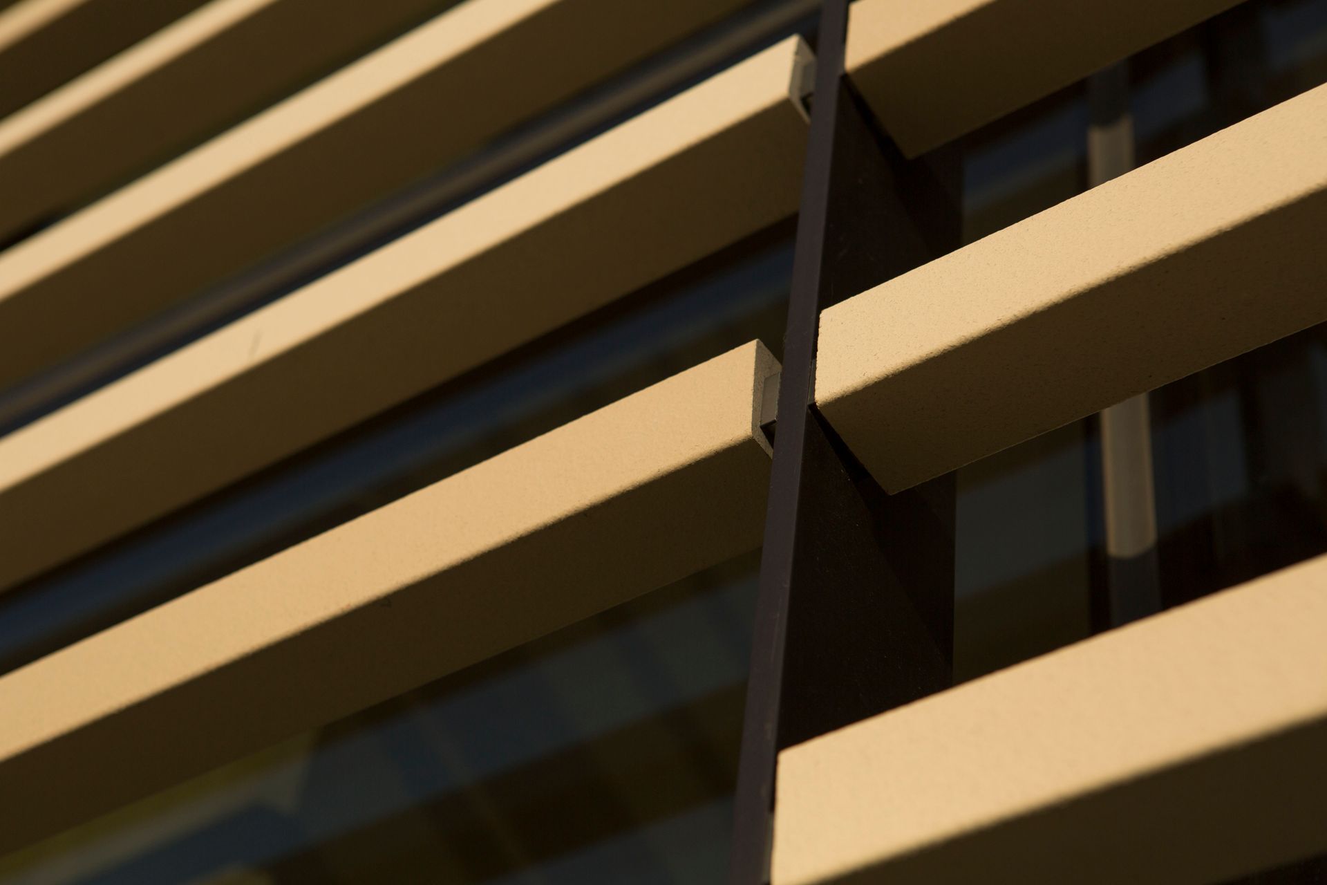 Exterior of a building with horizontal, beige-colored sunshades creating stripes of light and shadow.