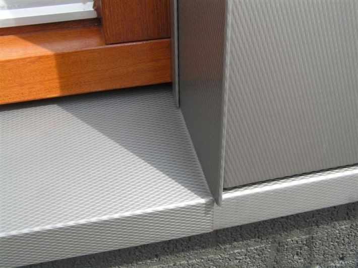 Close-up of a silver metal door threshold and frame with a textured surface, next to a wooden window frame.