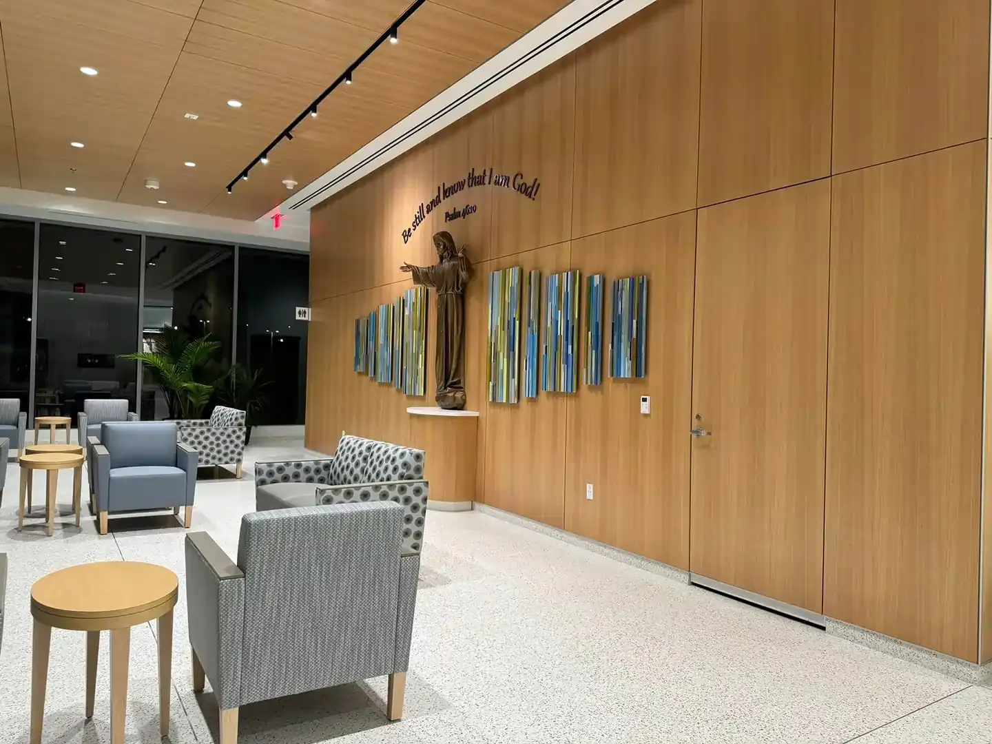 Lobby with wood-paneled wall, statue, and abstract art. Armchairs and small tables are arranged.