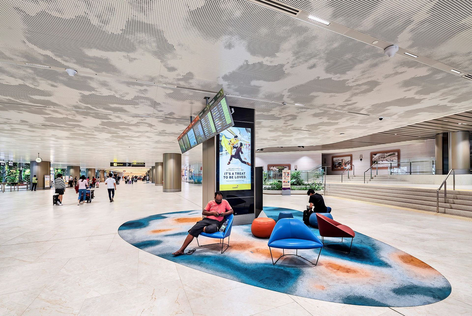 Airport interior with people, patterned ceiling, seating area, and digital displays.