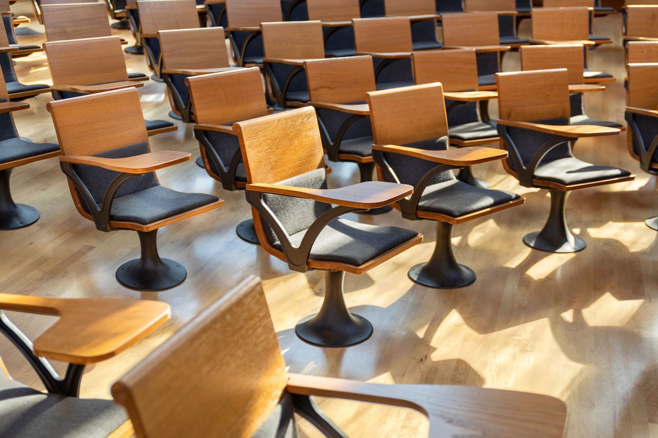 Rows of empty wooden lecture hall chairs with attached writing surfaces.