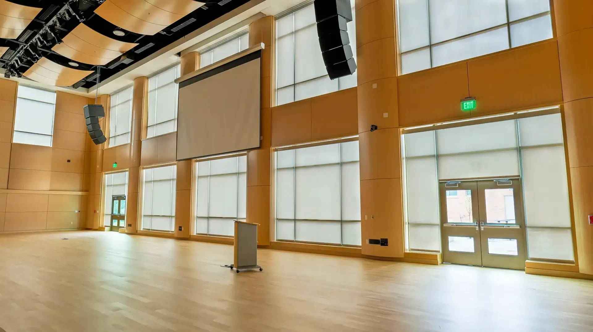 Empty event space with wood floor and ceiling, tall windows, and a projection screen.