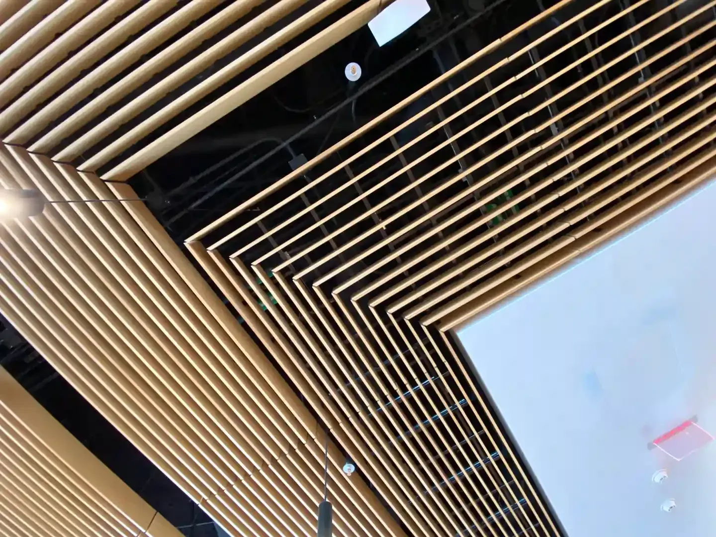 Angled wooden slats form a ceiling design, juxtaposed with a white wall.