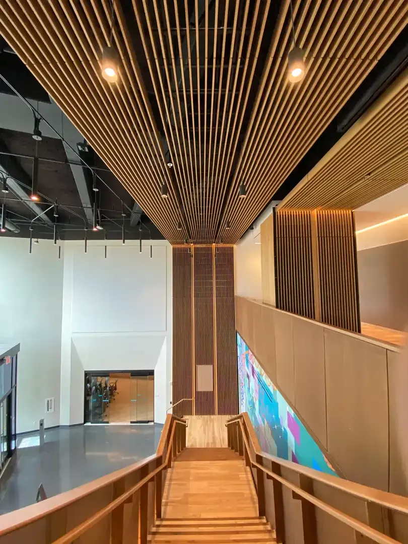 Wooden staircase and ribbed ceiling in a modern building; warm tones, indirect lighting.