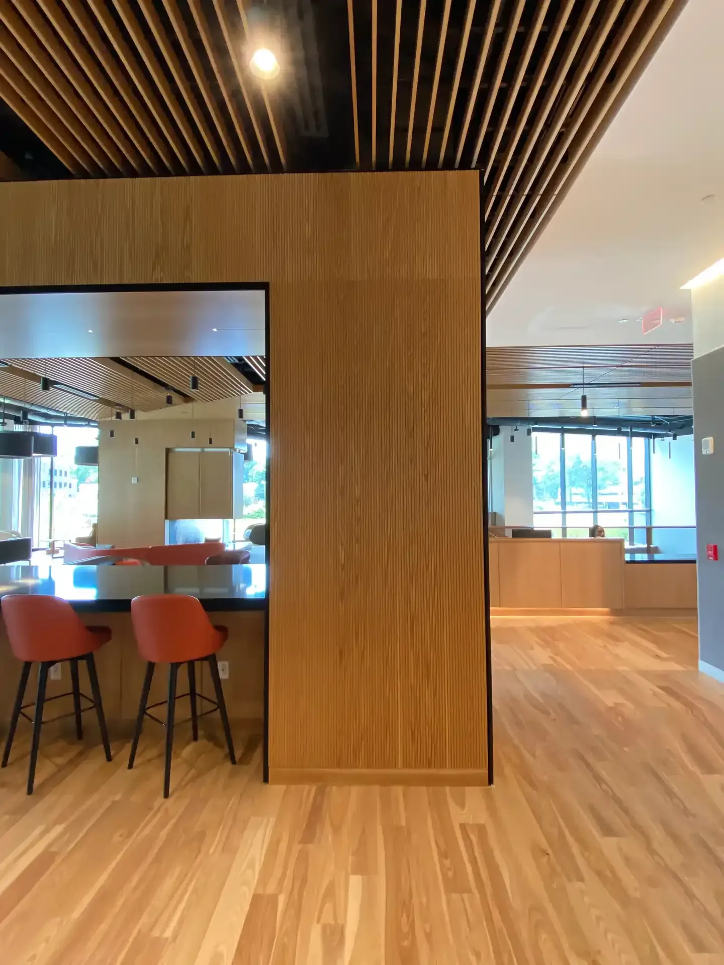 Modern interior: wood paneling, slatted ceiling, bar with orange stools, hardwood floors.