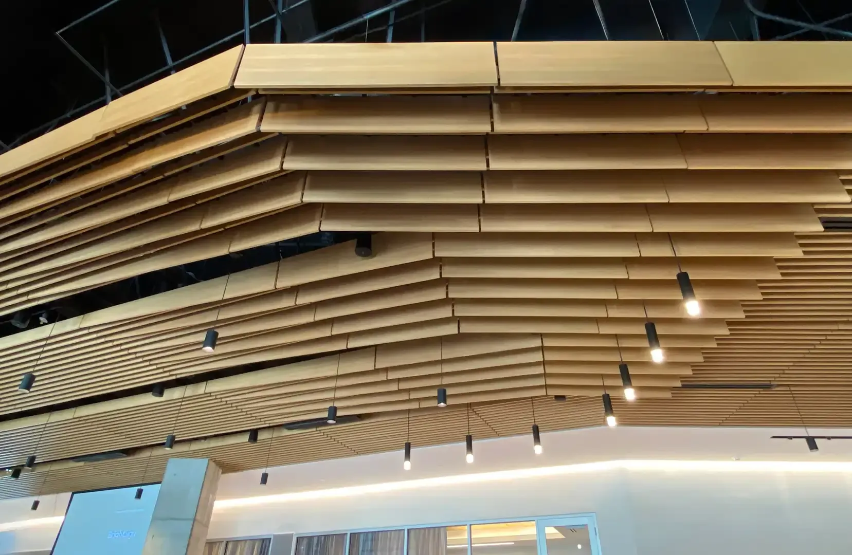 Wooden slatted ceiling with hanging lights, angled design, in a modern interior setting.