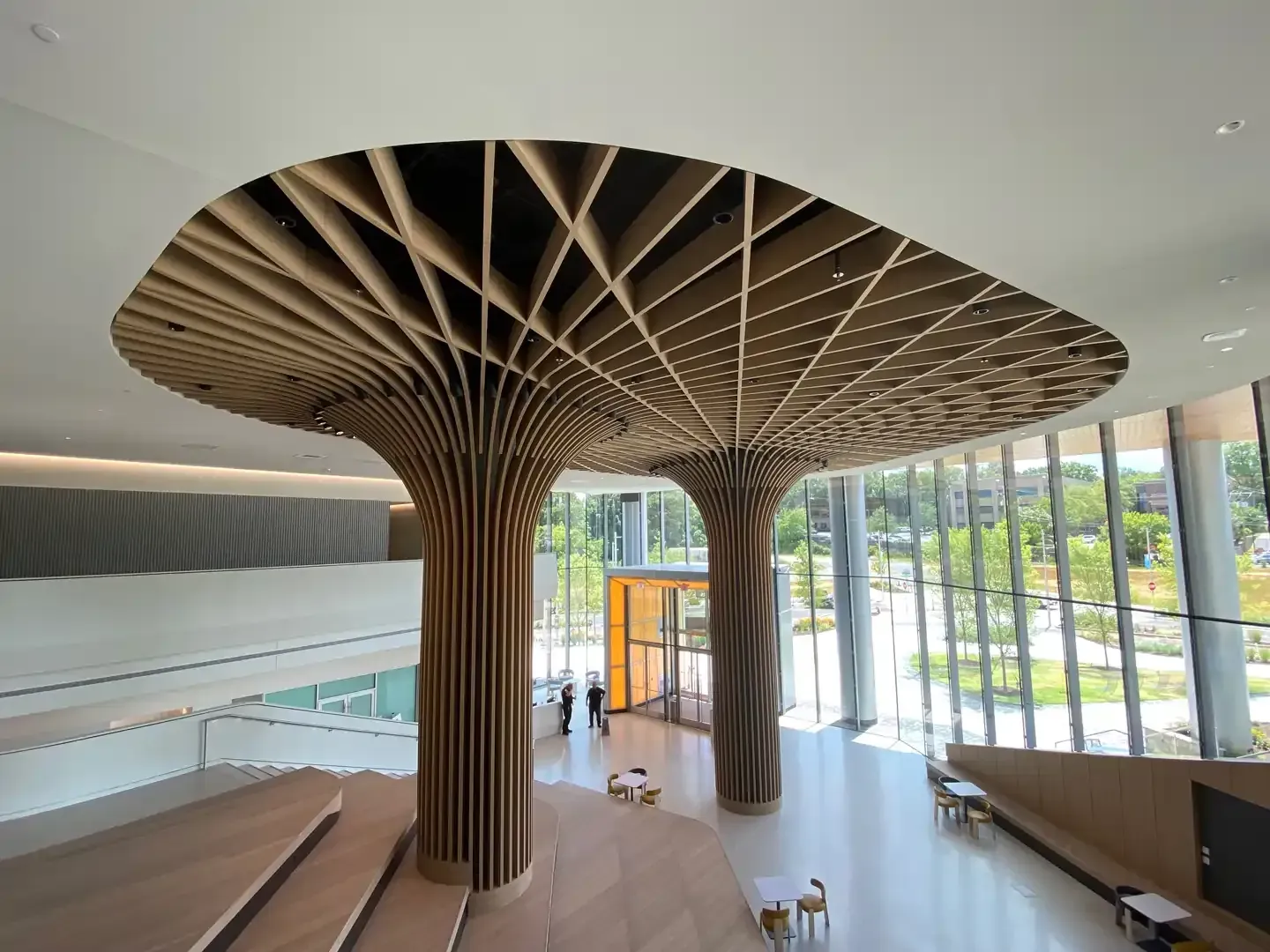 Wooden pillars support a latticed ceiling in a modern building. Sunlight streams through the glass windows.