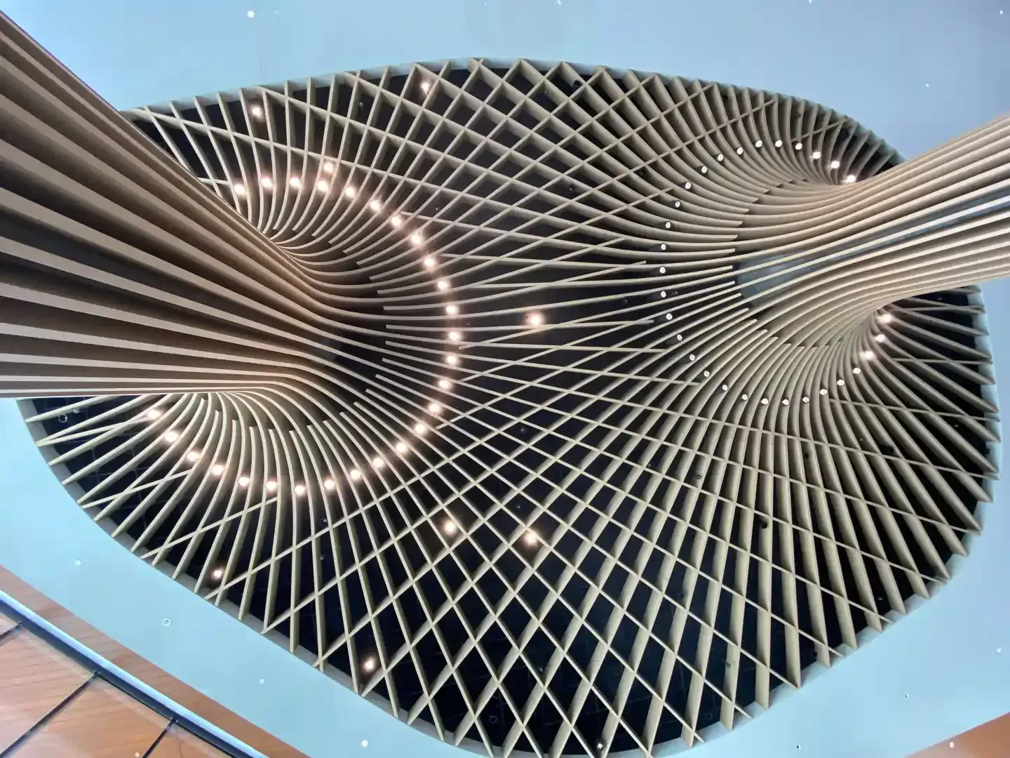 Architectural ceiling with swirling wooden beams, crisscrossed grid, and embedded lights.