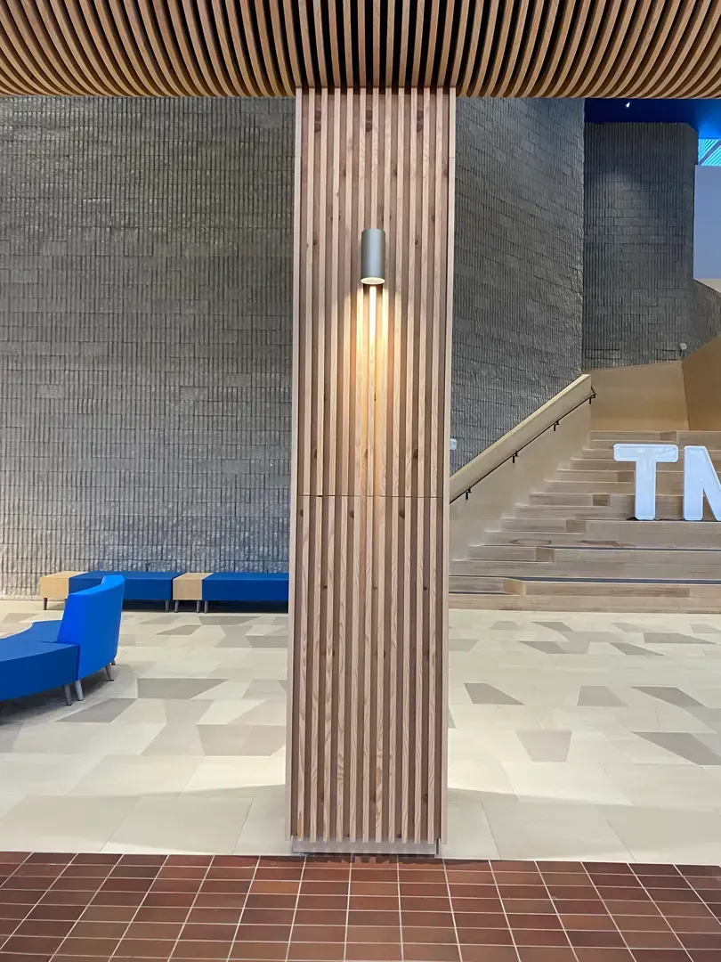 Wooden-paneled pillar with a light fixture, brick floor, and textured gray wall. Blue seating area and stairs visible.