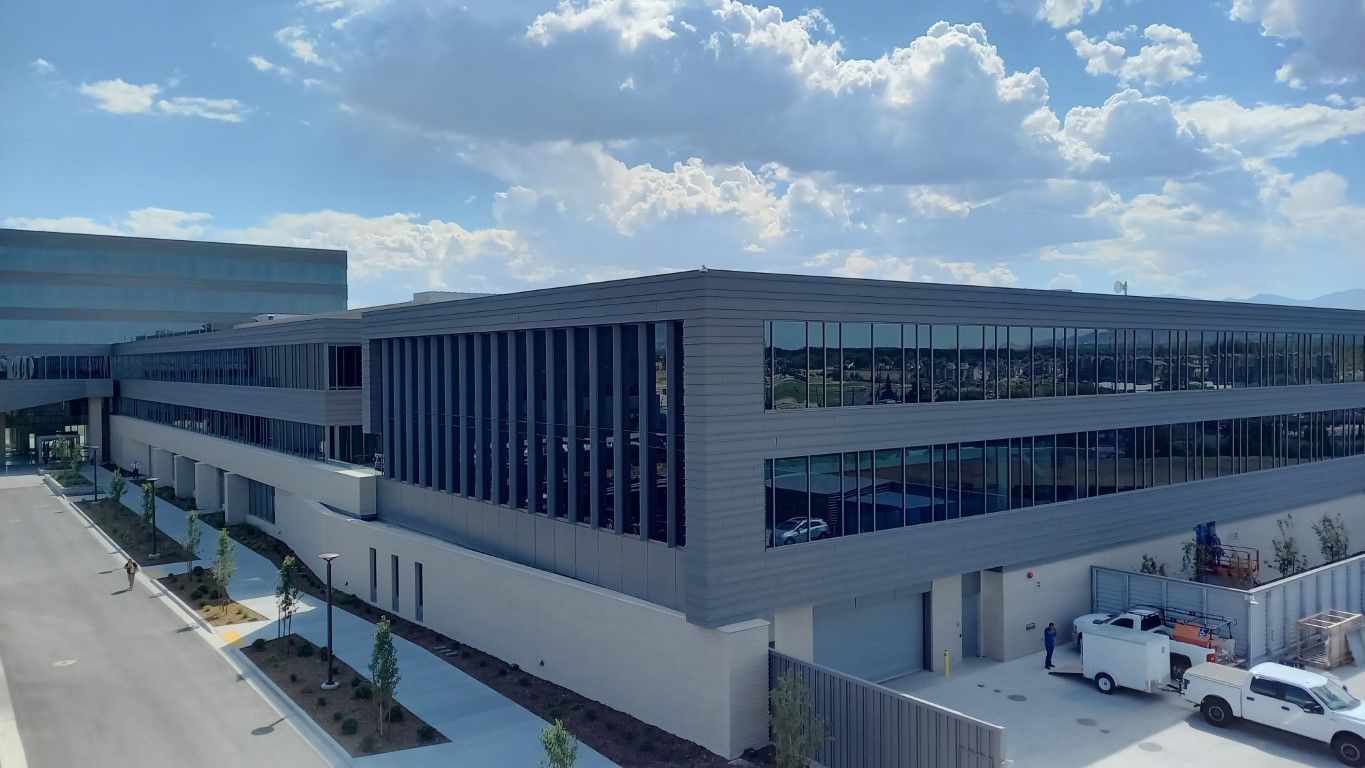 Modern, multi-story building with a flat roof, large windows, and a cloudy sky above.