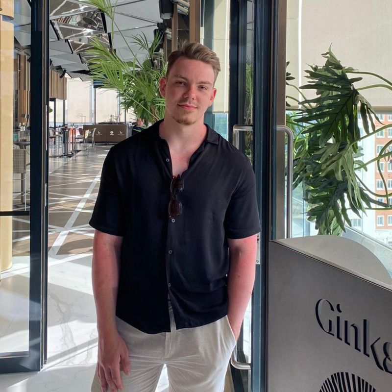 A person in a black short-sleeved button-down shirt and light-colored pants standing in a bright, modern indoor space.