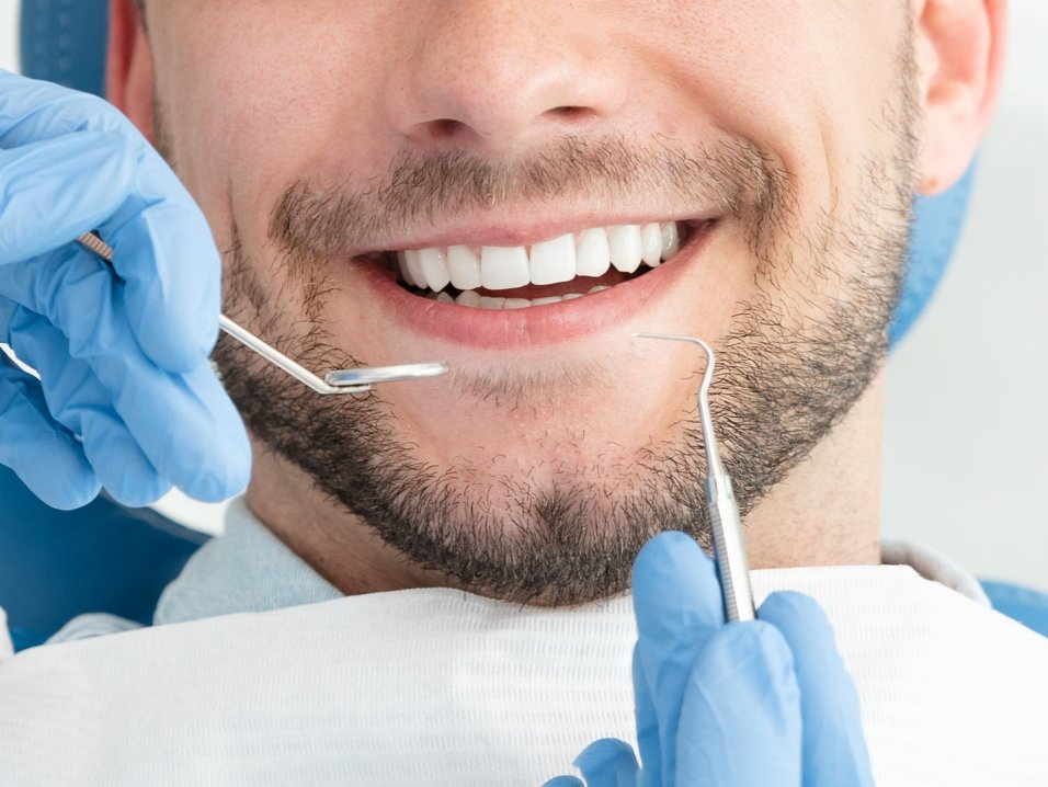 Dentist examining a patient's bright, white teeth with dental tools in a bright office.