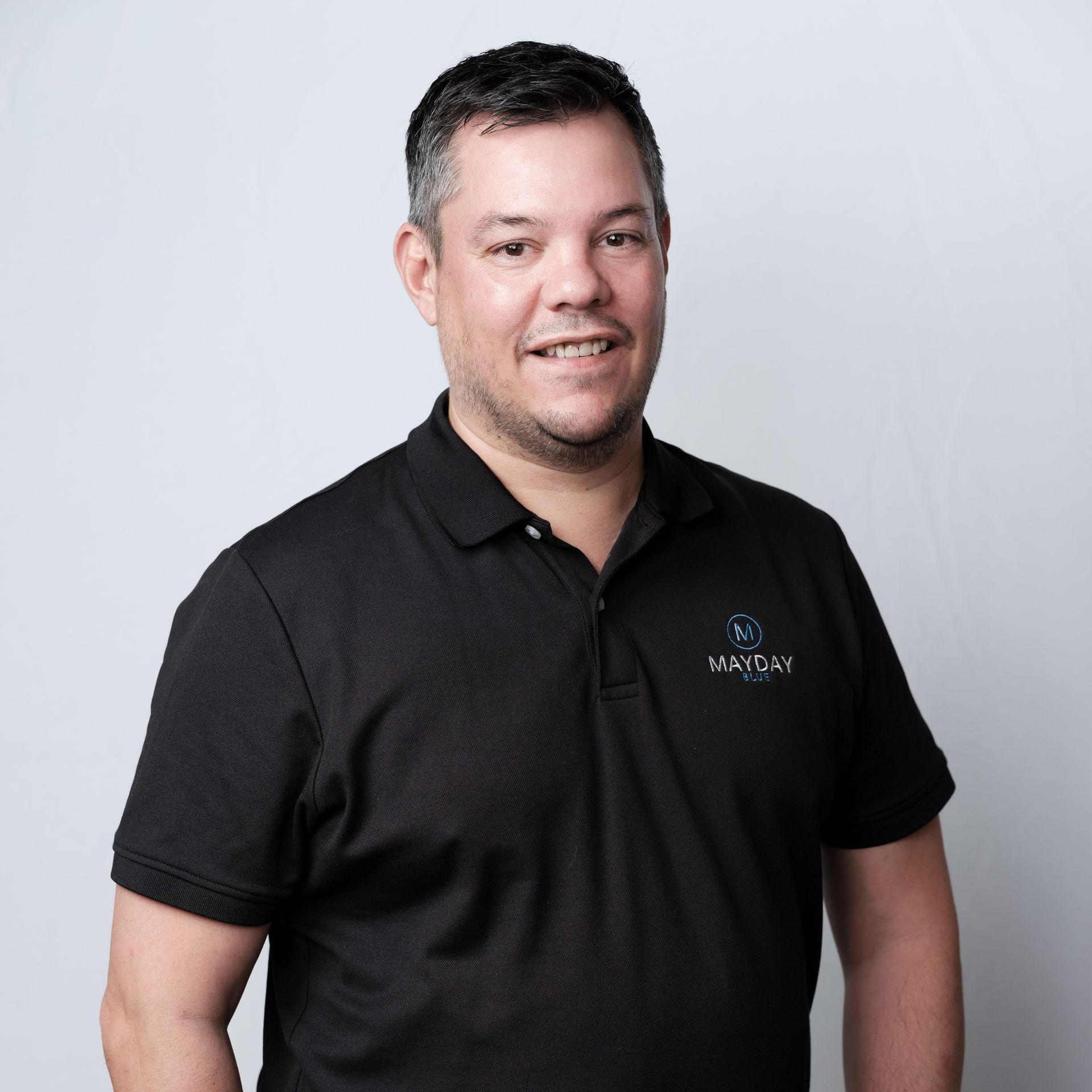 Man wearing a black polo shirt, smiling, posing in front of a white background.