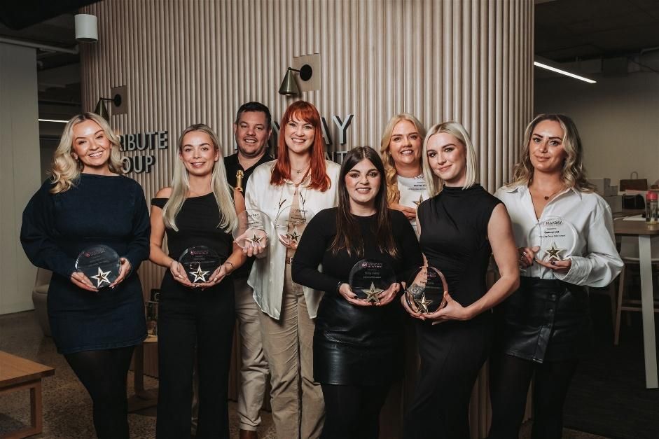 Group of people holding awards, posing in an office setting.