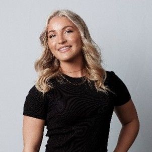 Woman with blonde hair wearing a black shirt, smiling against a light gray backdrop.