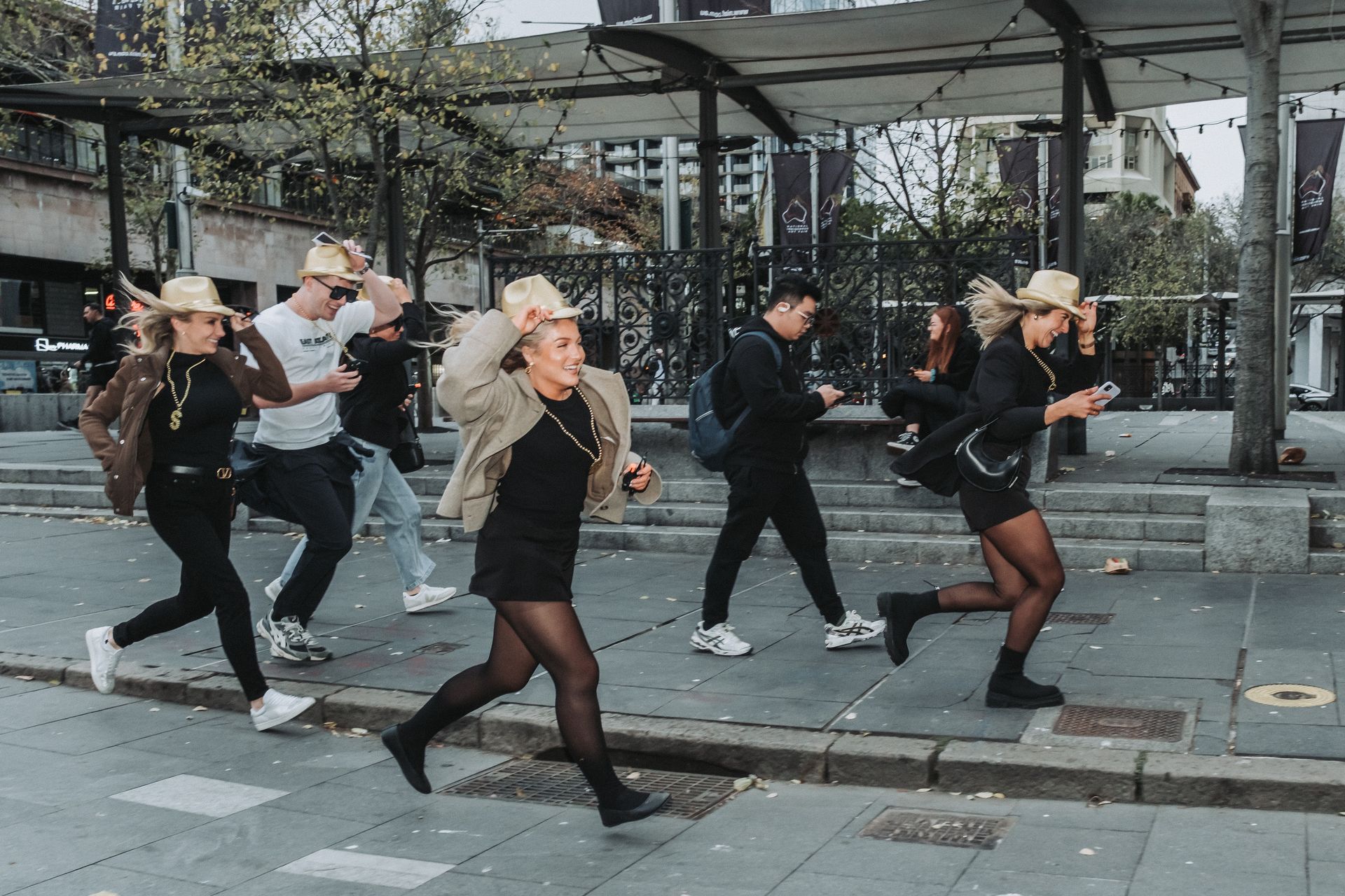 People running on a city street, some wearing hats and holding phones.