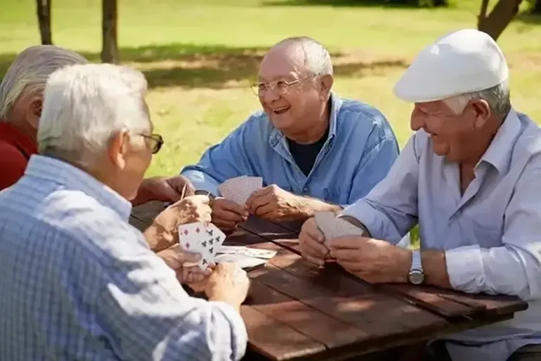 Four people playing cards at a picnic table in a sunny park