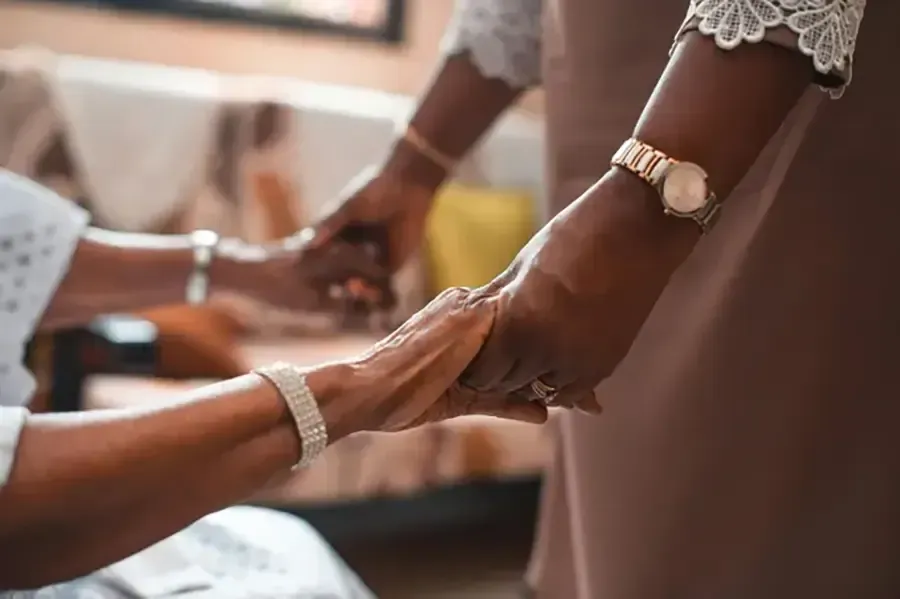 Hands gently holding in a warm indoor setting, with lace sleeves and a watch visible