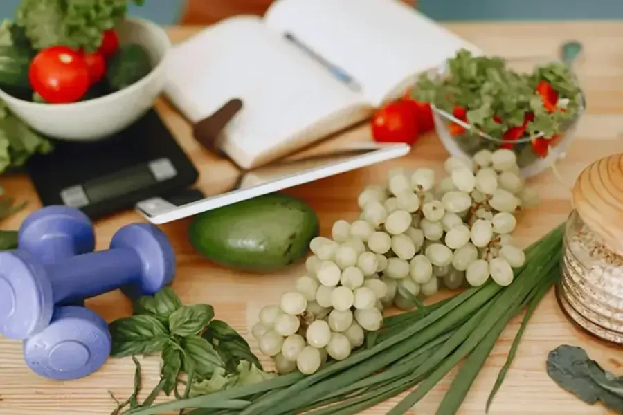 Still life of healthy foods, dumbbells, notebook, and plants on a table