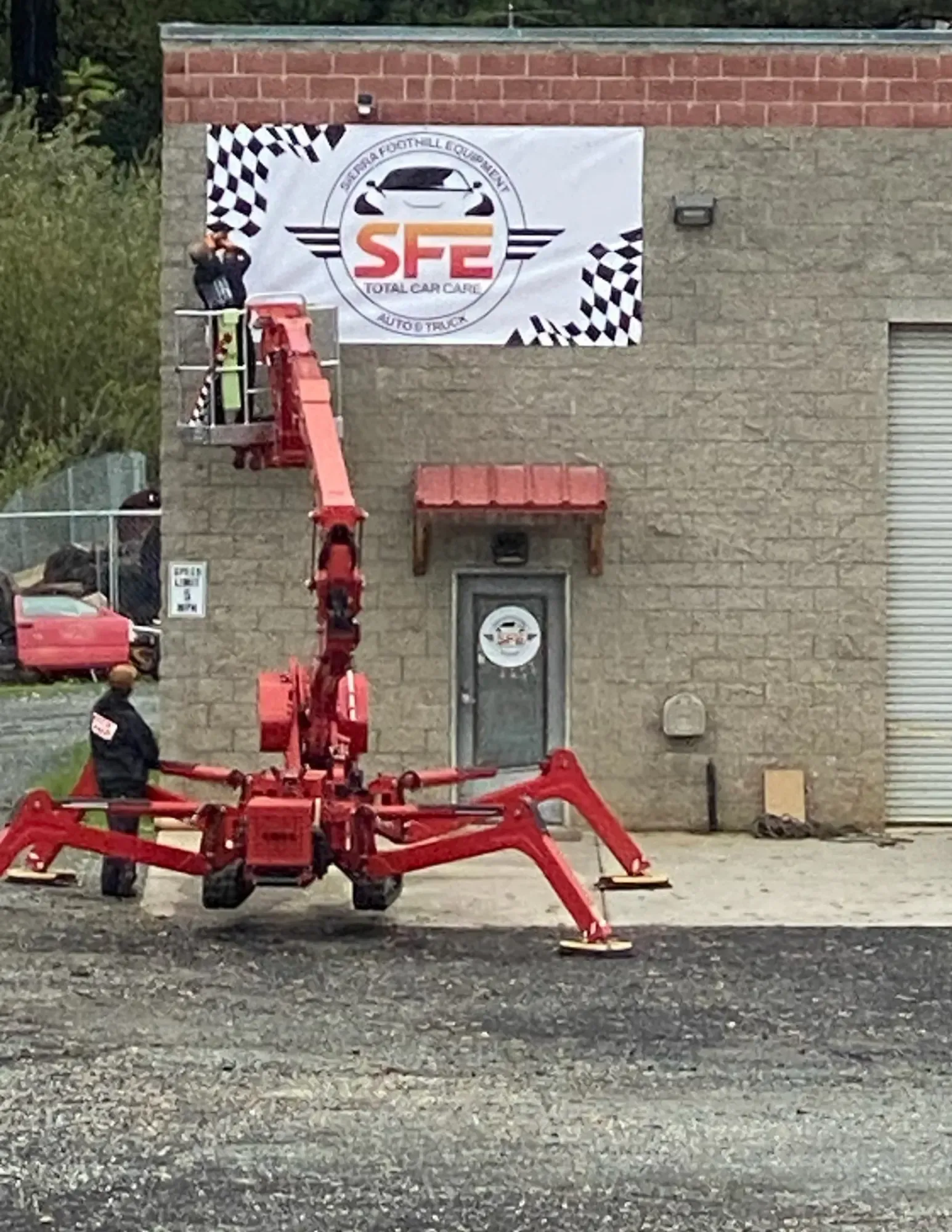 Two workers on a red lift installing a banner that reads