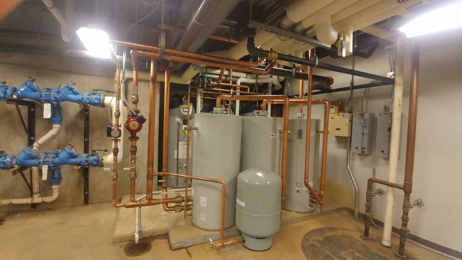 Pipes, tanks, and valves in a basement. Copper pipes, gray tanks, and blue valves are visible.