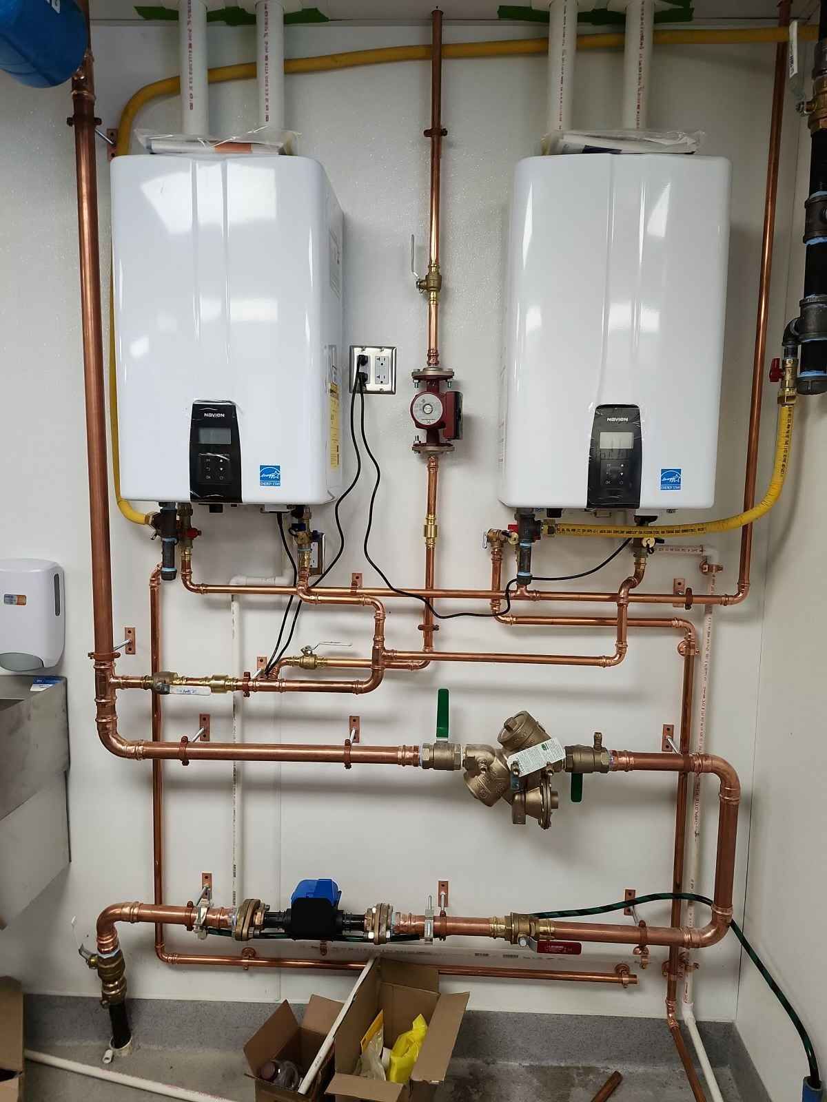 Two white tankless water heaters with copper pipes on a wall.