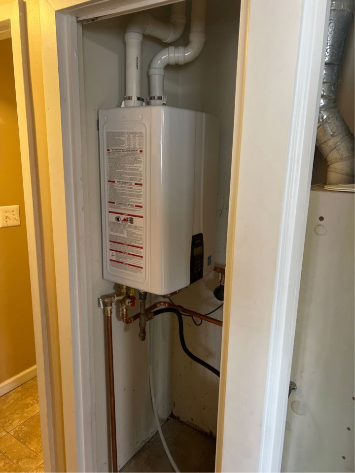 White tankless water heater in a closet, with white pipes and a metal flue.
