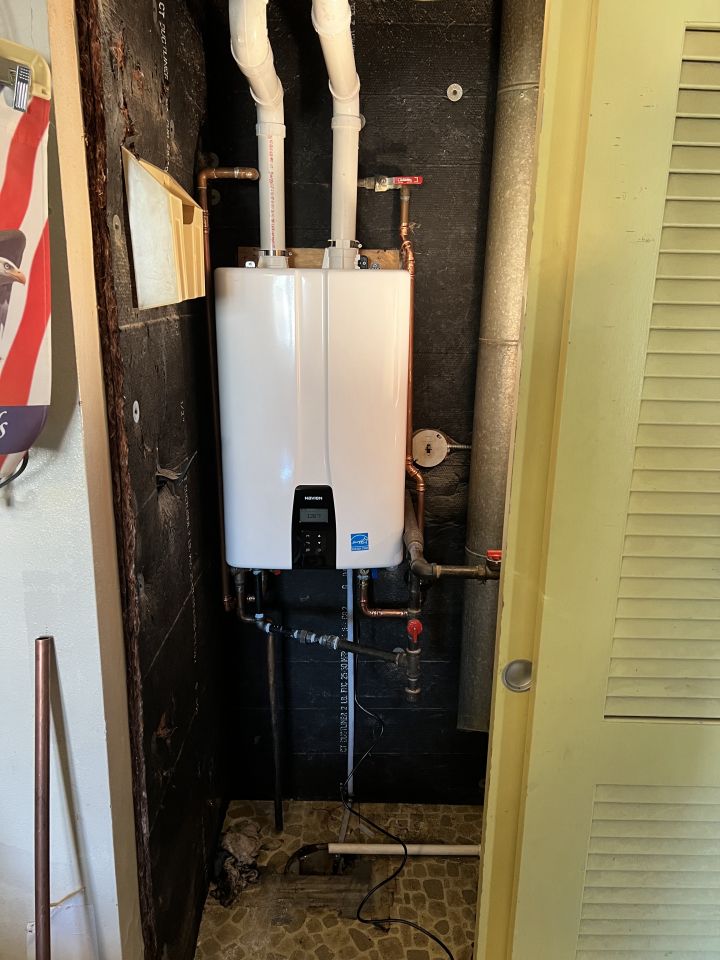 White tankless water heater installed in a small, dark closet, with copper pipes and white vent pipes.