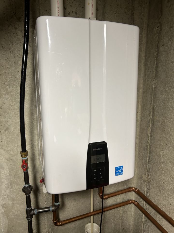 White wall-mounted water heater with digital display and copper pipes, installed on a concrete wall.