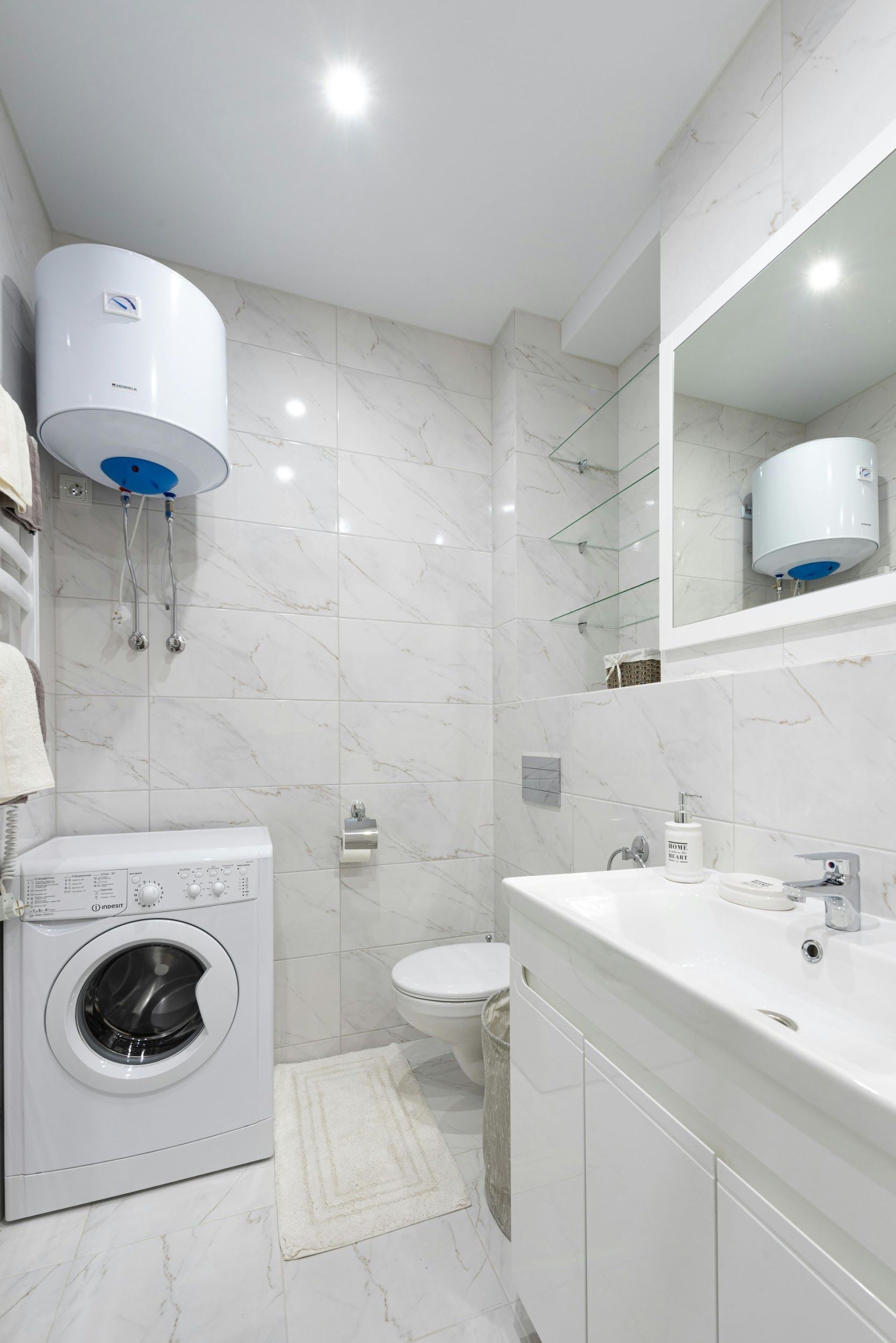 White bathroom with washing machine, water heater, toilet, sink, and mirror.