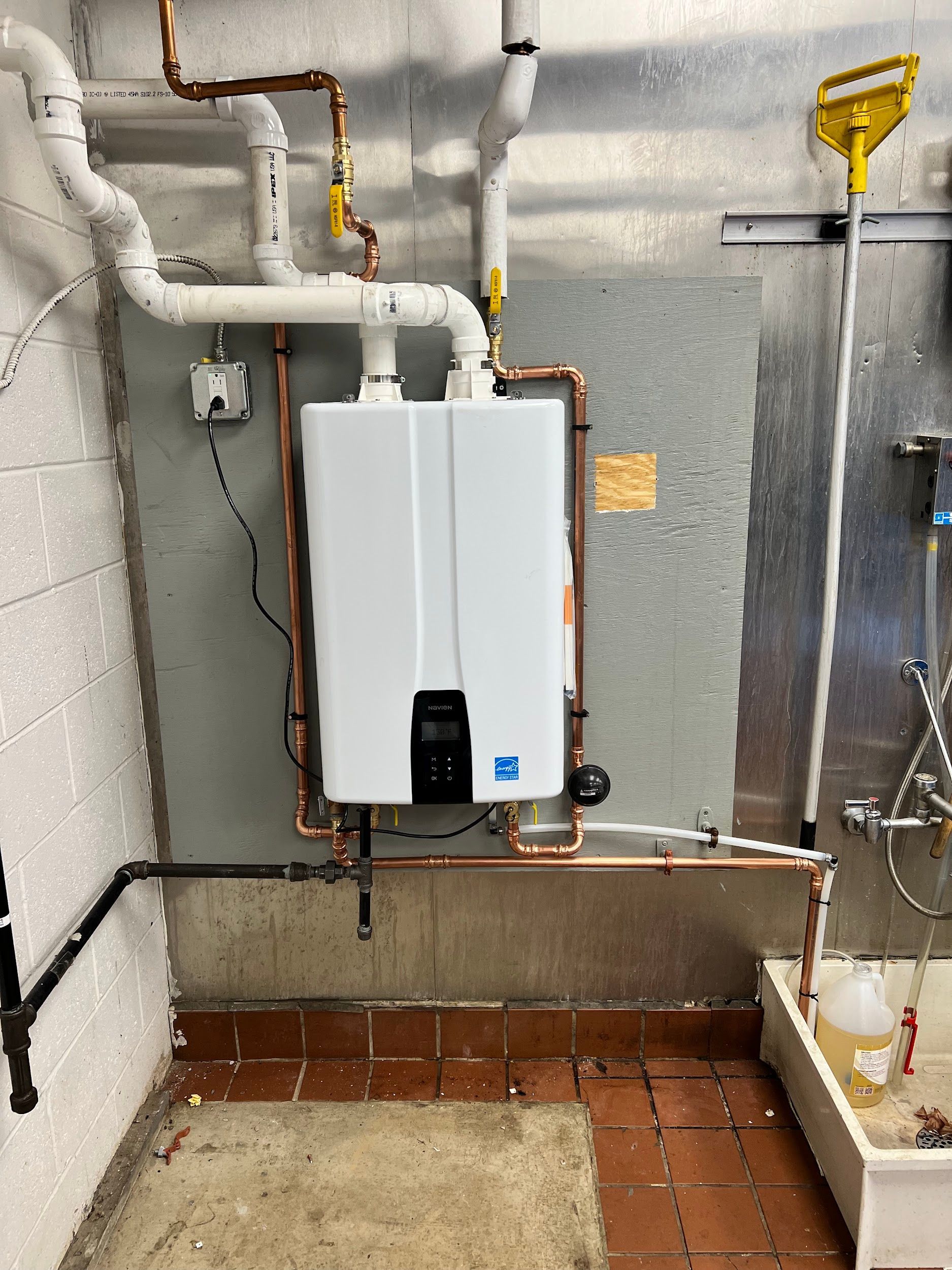 Tankless water heater installed on a wall with copper pipes. Located in an industrial setting.