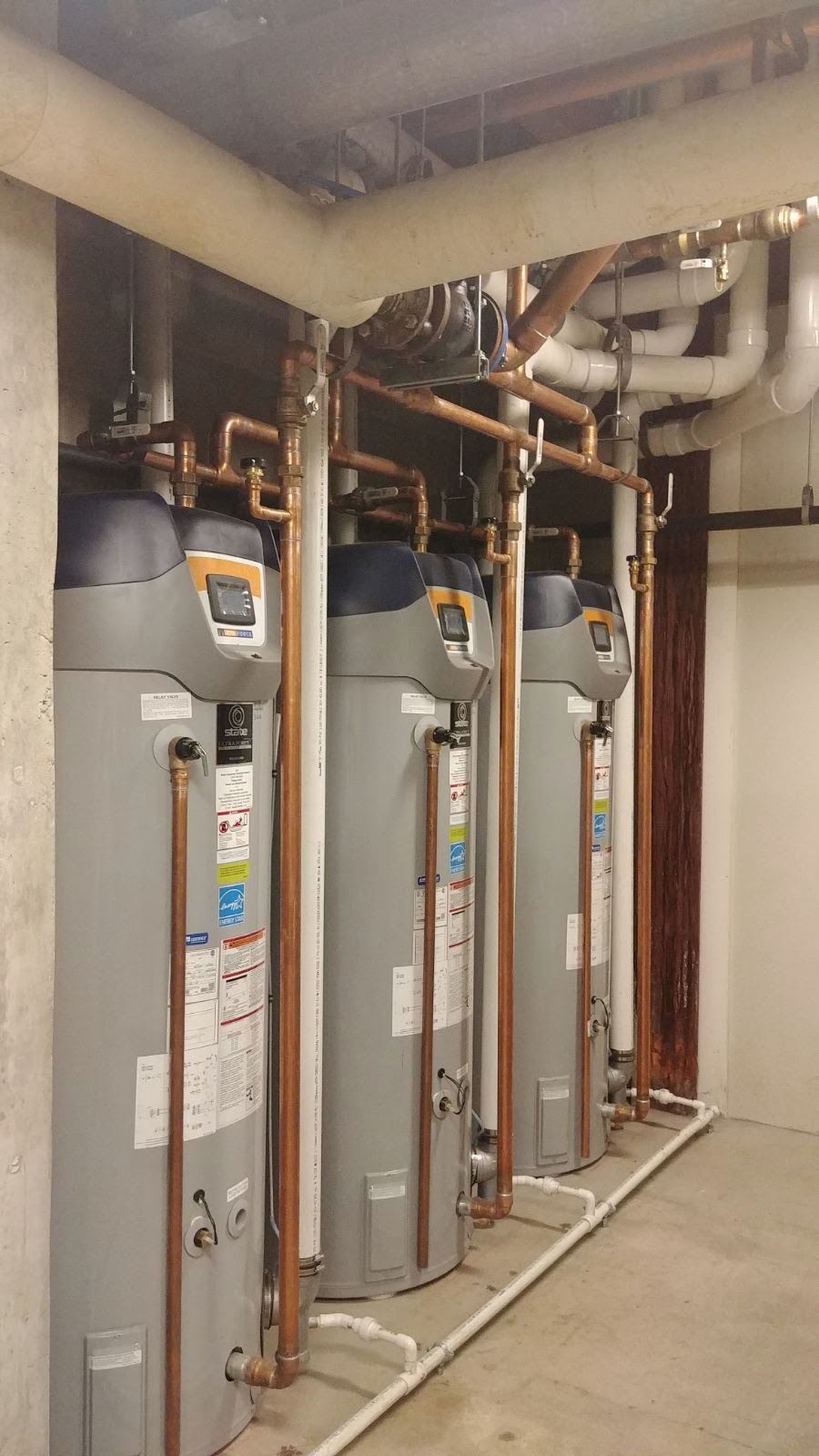 Three tall gray water heaters with copper pipes in a basement.