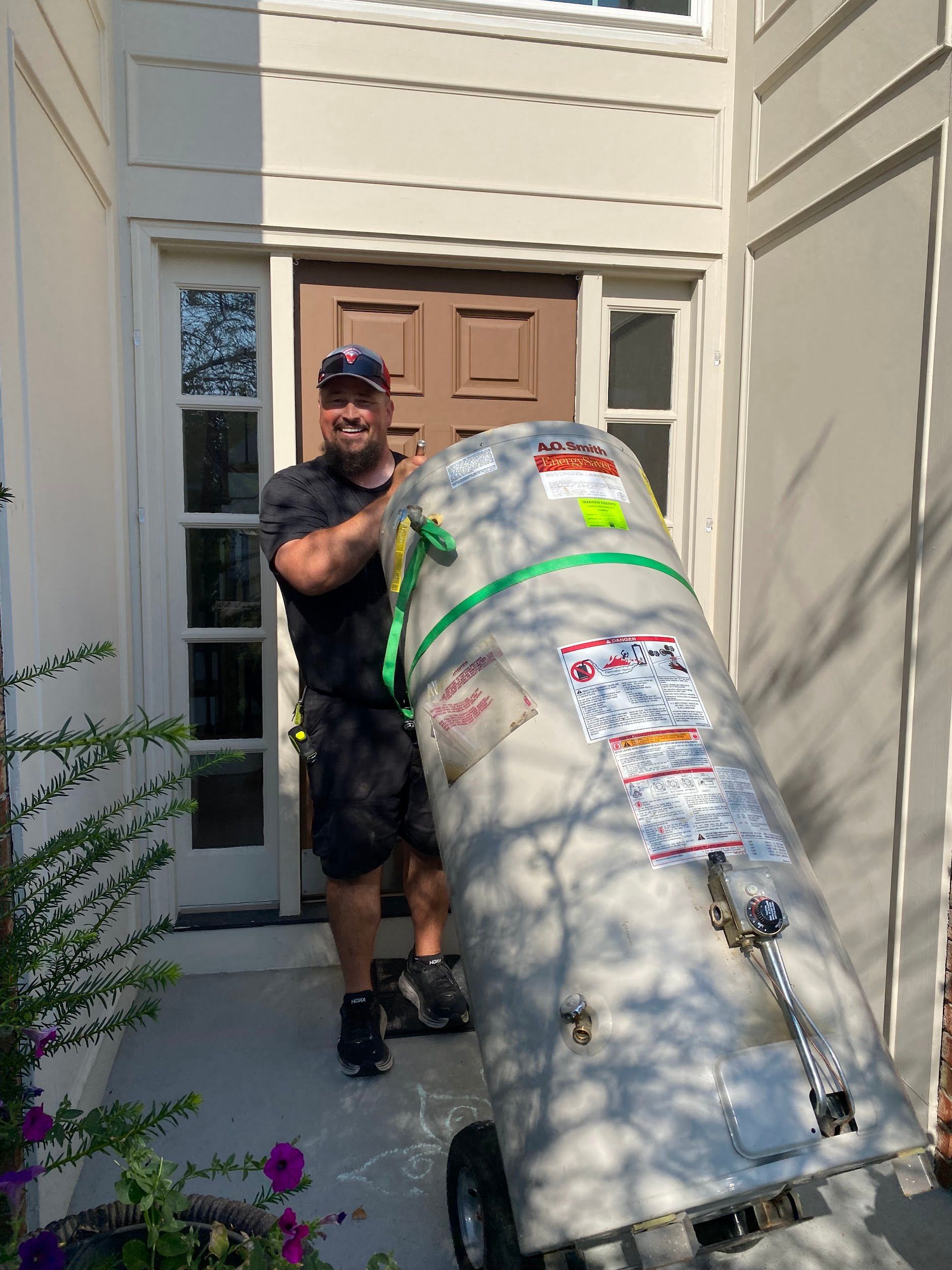 Man transporting a large water heater on a dolly outside a home.